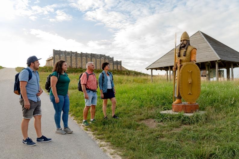 Eine Gruppe von Wanderern betrachtet die Holzfigur eines keltischen Kriegers beim Freilichtmuseum